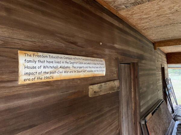 A wooden wall displays a sign about the Freedom Education Campus and the Dogtrot Odum family house history.